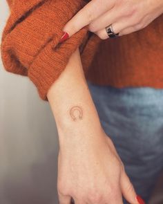 a woman's hand with a small tattoo on her left wrist and an orange sweater