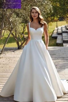 a woman in a white wedding dress is standing on a wooden walkway with trees and benches behind her