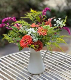 a white vase filled with lots of colorful flowers on top of a wooden table outside