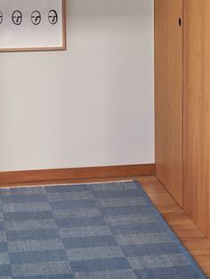 an empty room with a blue rug on the floor next to a wooden cabinet and door