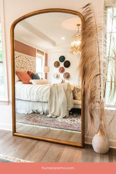 a large mirror sitting on top of a wooden floor next to a bed in a bedroom