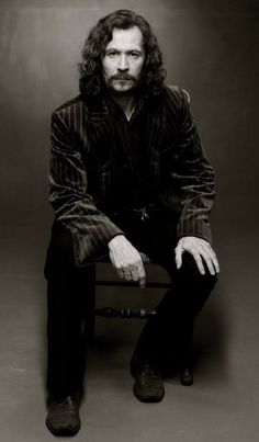 a man with long hair sitting on a chair in a black and white photo posing for the camera