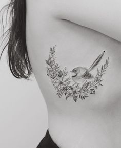 a woman's back with a bird and flowers tattoo on her left side ribcage