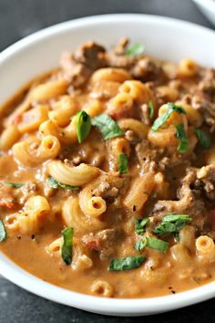 a white bowl filled with pasta and meat in tomato sauce, garnished with green leaves