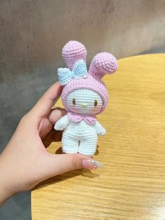 a hand holding a small crocheted bunny doll on a wooden table next to a person's finger