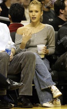 a woman sitting next to a man at a basketball game holding a drink and talking on the phone