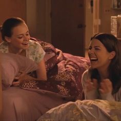 two women laughing while laying in bed together