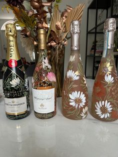 three bottles of wine are sitting on a table next to flowers and vases with leaves