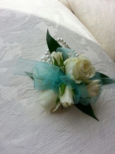 a boutonniere with white roses and blue ribbon on a tableclothed surface