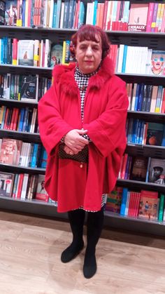 a woman standing in front of a bookshelf wearing a red coat and black boots