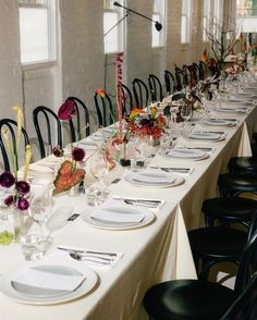 a long table is set with white plates and black chairs