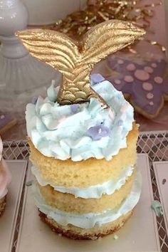 two cupcakes with frosting and gold decorations on top, one in the shape of a mermaid tail