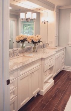 a white bathroom with two sinks and vases on the counter in front of it