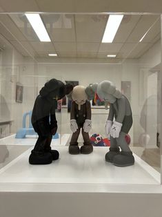 three figurines are on display in a glass case, one is touching the other's head