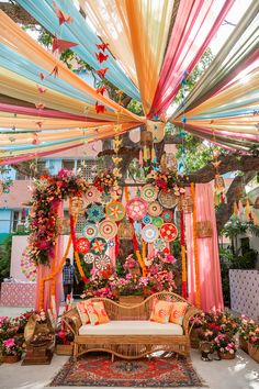 an outdoor seating area decorated with colorful ribbons and paper flowers on the ceiling, surrounded by potted plants