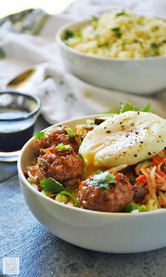 a white bowl filled with meat and vegetables next to a cup of sauce on the side