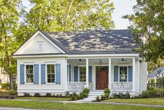 a white house with blue shutters on the front and side windows, surrounded by trees