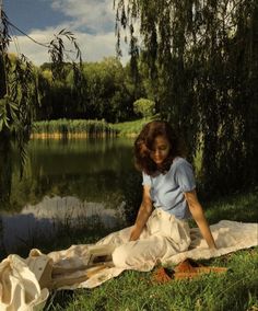 a woman sitting on top of a blanket next to a lake