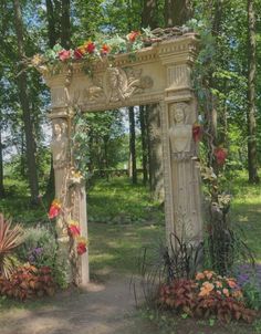 an arch with flowers on it in the middle of a park area surrounded by trees