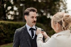 a man in a suit and tie is fixing another mans bowtie on his neck