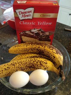 two bananas and three eggs in a glass bowl on a counter next to a box of cheesecakes