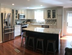 a kitchen with stainless steel appliances and white cabinets is pictured in this image, there are stools at the center of the island