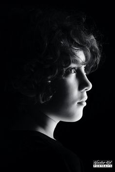 a black and white photo of a woman's face with curly hair in the dark