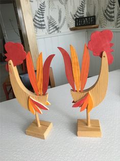 two wooden roosters sitting on top of a table next to each other with red and orange feathers