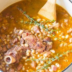 a pot filled with beans and meat next to a wooden spoon