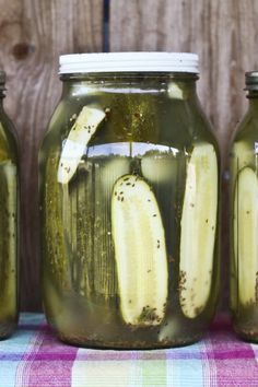 three jars filled with pickles sitting on top of a checkered table cloth next to each other