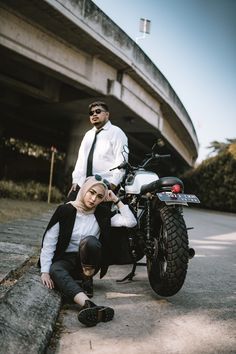 two people sitting on the ground next to a motorcycle