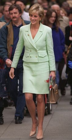 the woman is walking down the street with her hand in her pockets and wearing a light green suit