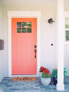 an orange front door with two potted plants on the side and a welcome mat