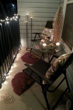 a small balcony with candles and lights on the railing, next to a table that has two chairs in front of it