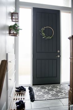 a black front door with a wreath on it and some shoes in the foreground