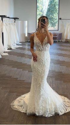 a woman taking a selfie in a wedding dress shop with her phone up to her face