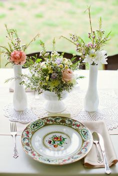 the table is set with flowers in vases, plates and utensils on it