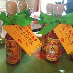 three bottles of hot sauce with green bows on them sitting on a counter top next to wine glasses