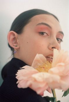 a woman holding a flower up to her face with one eye open and the other half closed