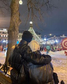 two people sitting on a bench in front of a christmas tree with lights and decorations