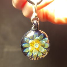 a hand holding a glass bead with a yellow flower on it's end