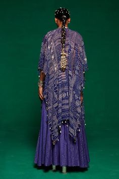 Purplish blue cape with tribal geometric print and thread, mirror, shell tassel embroidery. Paired with embroidered padded waistcoat and polka dot woven sharara.
Components: 3
Pattern: Printed, Embroidery
Type Of Work: Geometric tribal, thread, mirror, shell tassel
Neckline: Cape: Open, Waistcoat: V neck
Sleeve Type: Flared sleeves
Fabric: Muslin, Georgette, Dotted Chanderi
Color: Purple,Blue
Other Details: 
Metal coin and tassel embellished border
Approx. product weight: 5-7 kgs 
Occasion: Sang Bohemian Georgette Sharara For Navratri, Bohemian Chanderi Sets With Long Sleeves, Festive Bohemian Sharara With Traditional Drape, Bohemian Long Sleeve Chanderi Sets, Festive Bohemian Sharara, Bohemian Sharara With Traditional Drape, Bohemian Designer Traditional Wear In Georgette, Bohemian Semi-stitched Sharara With Sheer Dupatta, Bohemian Georgette Festive Sets