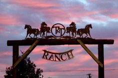 a sign that says ranch with horses on it and the sky is pink in the background