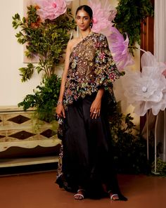 Feel the Summer breeze in this one-shoulder kaftan set. The cape is worn over a halter-neck gold top which appears as if it was dipped in gold while the black cape carries a bouquet of flowers embroidered on it. The flowy and comfortable pants and top together look regal as well as flowy to beat the heat. Halterneck blouse with a dori for closure at the back. Floral embroidered one-shoulder black cape. Basic black pants come with a simple flowy look and an SS concealed zip for a seamless look. F Cape And Pants, One Shoulder Sequin Evening Sets, One-shoulder Sequin Set For Party, One Shoulder Sequin Set For Party, Festive Off-shoulder Party Sets, Elegant One Shoulder Dress With Sheer Dupatta, Elegant One-shoulder Sequin Set, Festive One-shoulder Evening Sets, Black Sets With Cape Sleeves For Evening