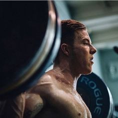 a man with no shirt is holding a barbell in his hand and looking off into the distance