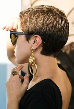 a woman with short hair and sunglasses on her head looking off into the distance while wearing gold hoop earrings