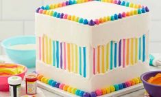 a large multi colored cake sitting on top of a table next to bowls and utensils