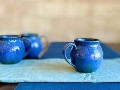 two blue mugs sitting on top of a table next to a napkin and bowl