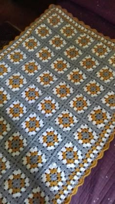 a crocheted blanket sitting on top of a purple bed next to a pillow