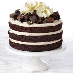 a chocolate cake with white frosting and flowers on top is sitting on a pedestal